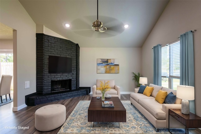 living room with ceiling fan, lofted ceiling, a brick fireplace, and dark wood-type flooring