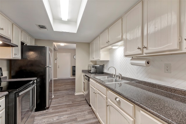 kitchen with appliances with stainless steel finishes, decorative backsplash, light hardwood / wood-style floors, white cabinets, and sink