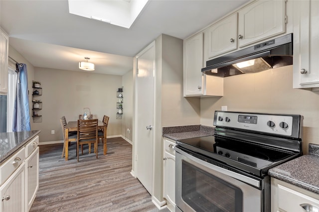 kitchen with white cabinets, light hardwood / wood-style floors, stainless steel electric range oven, and a skylight