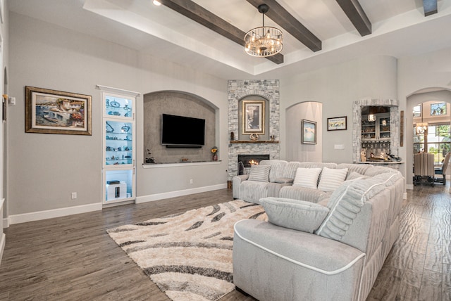 living room featuring a notable chandelier, beam ceiling, dark hardwood / wood-style flooring, and a stone fireplace