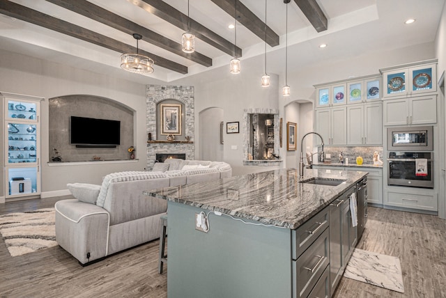 kitchen with pendant lighting, a kitchen island with sink, sink, stainless steel appliances, and a large fireplace