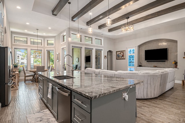 kitchen featuring pendant lighting, an island with sink, sink, stone countertops, and appliances with stainless steel finishes