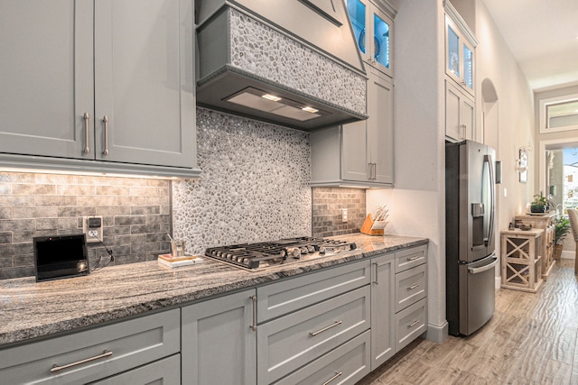 kitchen with appliances with stainless steel finishes, light hardwood / wood-style floors, light stone counters, gray cabinets, and custom exhaust hood