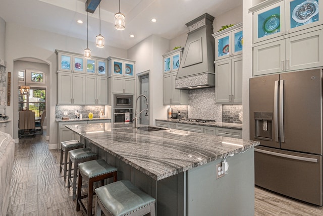 kitchen with light wood-type flooring, sink, stainless steel appliances, a center island with sink, and premium range hood