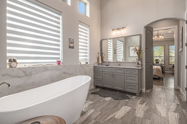 bathroom with an inviting chandelier, vanity, a tub to relax in, and a high ceiling