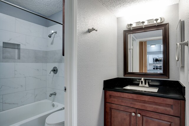 full bathroom featuring a textured ceiling, vanity, toilet, and tiled shower / bath