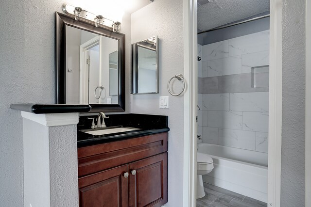 full bathroom with a textured ceiling, hardwood / wood-style flooring, tiled shower / bath combo, vanity, and toilet