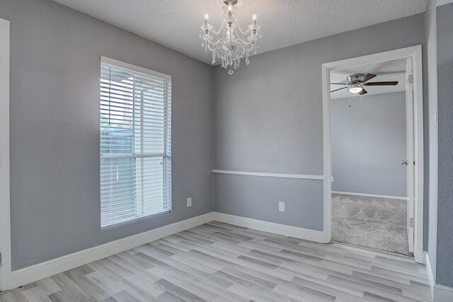 empty room with a textured ceiling, ceiling fan with notable chandelier, and light hardwood / wood-style flooring