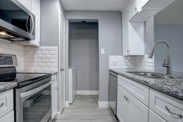 kitchen featuring sink, backsplash, white cabinetry, stainless steel appliances, and light stone countertops