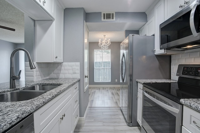 kitchen with a textured ceiling, decorative backsplash, white cabinetry, and stainless steel appliances