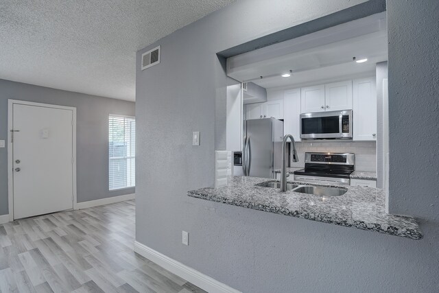 kitchen featuring light hardwood / wood-style floors, white cabinetry, light stone countertops, and stainless steel appliances