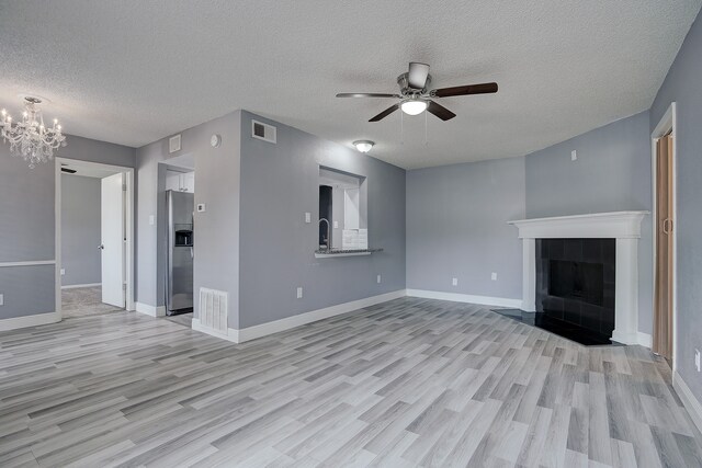 unfurnished living room with ceiling fan with notable chandelier, a textured ceiling, a fireplace, and light hardwood / wood-style floors