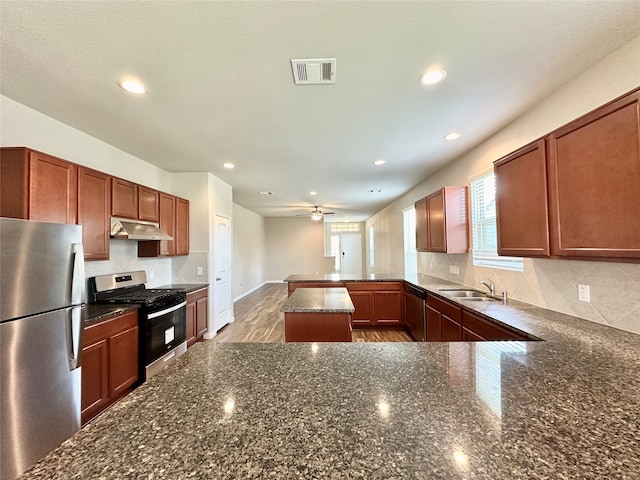 kitchen featuring ceiling fan, kitchen peninsula, light hardwood / wood-style flooring, appliances with stainless steel finishes, and dark stone countertops