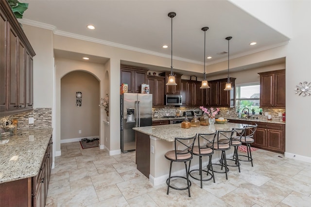 kitchen with light stone counters, a kitchen island, stainless steel appliances, backsplash, and decorative light fixtures