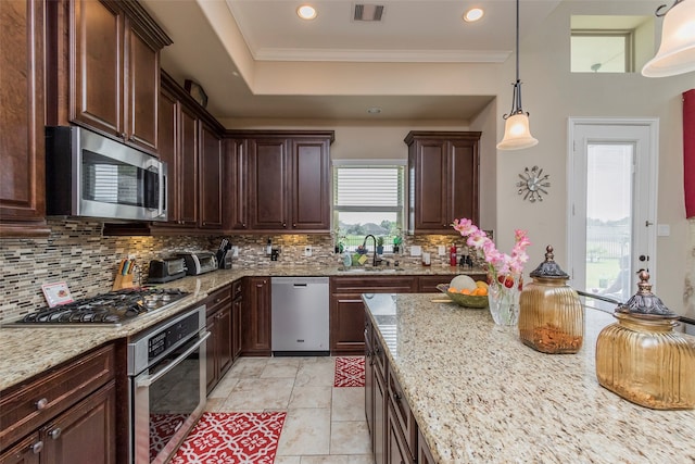 kitchen with pendant lighting, sink, backsplash, stainless steel appliances, and light stone countertops