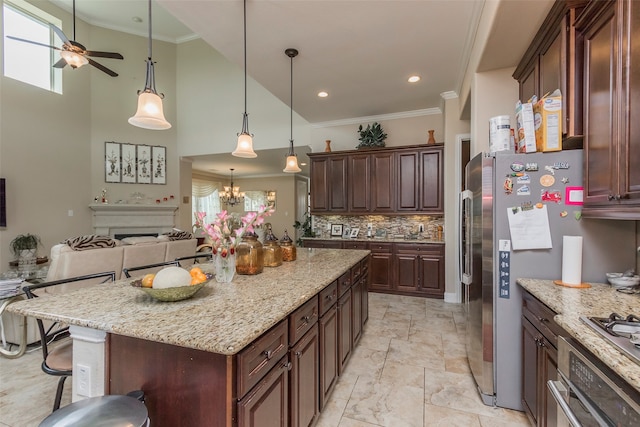 kitchen with light stone counters, a center island, a breakfast bar area, ceiling fan with notable chandelier, and ornamental molding