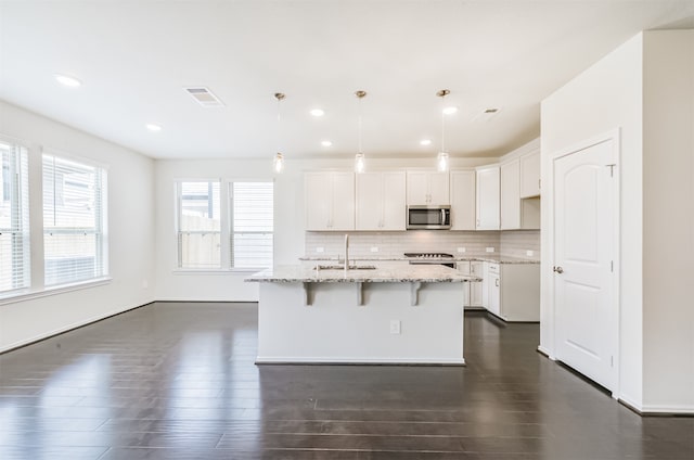 kitchen featuring appliances with stainless steel finishes, white cabinetry, pendant lighting, and light stone counters