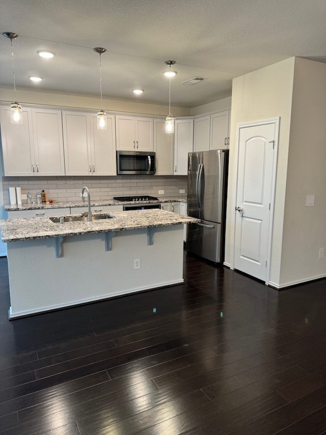 kitchen featuring pendant lighting, light stone counters, appliances with stainless steel finishes, and white cabinetry