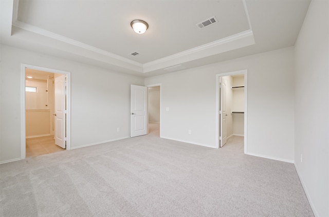 unfurnished bedroom with a tray ceiling, a closet, light colored carpet, ensuite bathroom, and a spacious closet