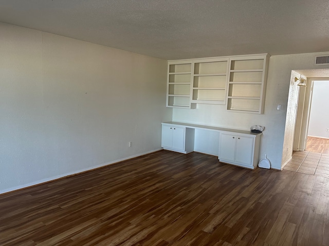 interior space featuring built in desk, a textured ceiling, and dark wood-type flooring