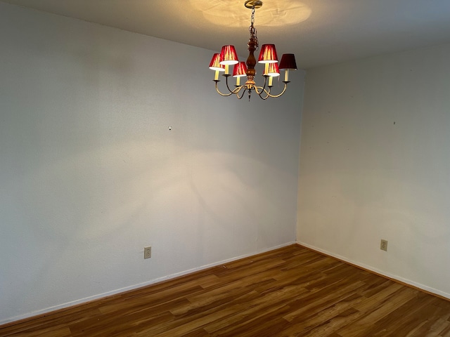 empty room featuring an inviting chandelier and dark hardwood / wood-style flooring