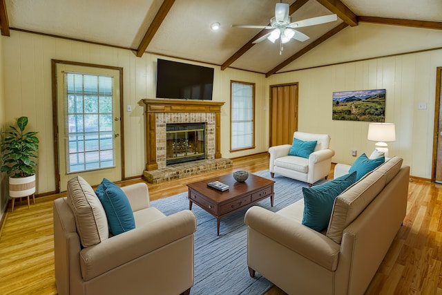 living room featuring ceiling fan, vaulted ceiling with beams, wooden walls, a fireplace, and light hardwood / wood-style floors