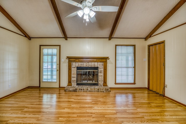 unfurnished living room with light wood-type flooring, a fireplace, lofted ceiling with beams, and ceiling fan