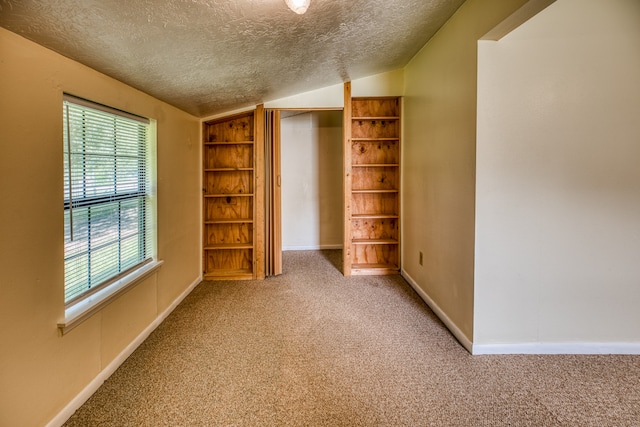 empty room with carpet, vaulted ceiling, a textured ceiling, and built in features