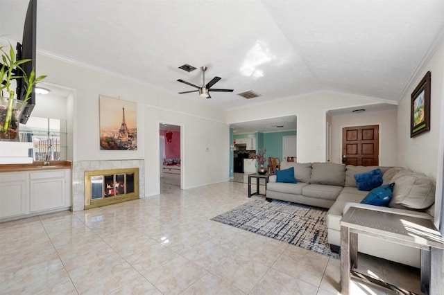 living room featuring a tile fireplace, lofted ceiling, crown molding, and ceiling fan