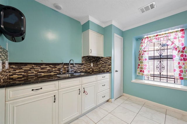 kitchen with sink, white cabinetry, dark stone countertops, crown molding, and decorative backsplash