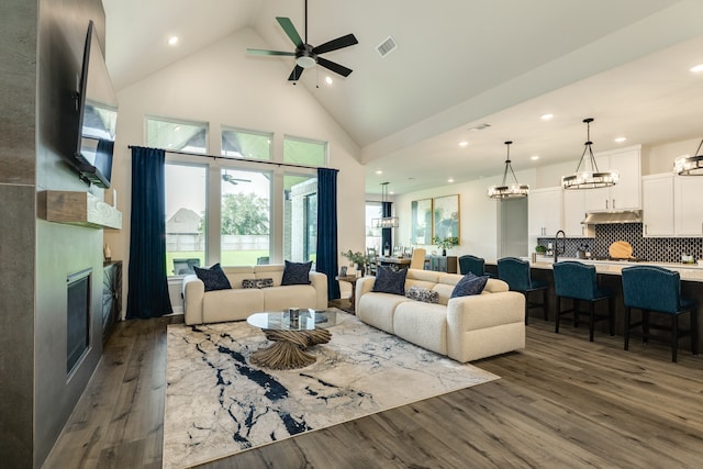 living room featuring ceiling fan with notable chandelier, dark hardwood / wood-style floors, sink, and high vaulted ceiling