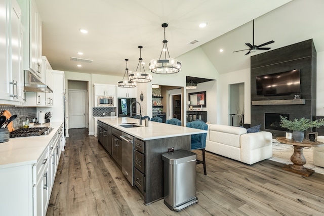 kitchen featuring white cabinets, ceiling fan with notable chandelier, a fireplace, a center island with sink, and sink