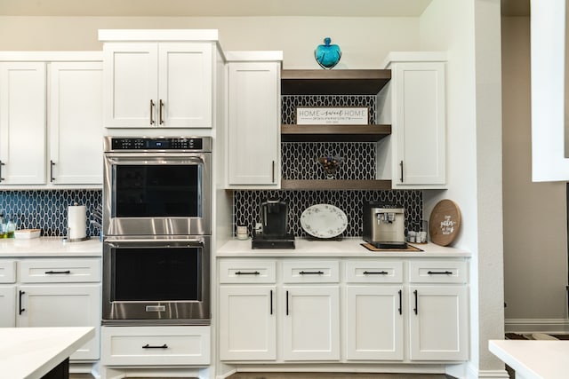 kitchen featuring stainless steel double oven, backsplash, and white cabinetry