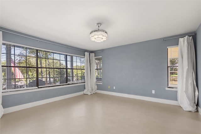 empty room with an inviting chandelier, concrete flooring, and plenty of natural light