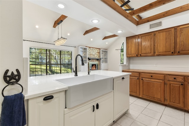 kitchen with a fireplace, light tile patterned floors, ceiling fan, vaulted ceiling with beams, and sink