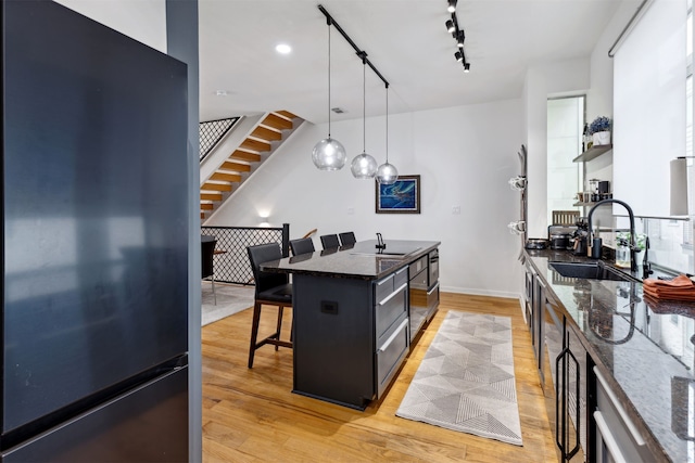 kitchen with a breakfast bar, black refrigerator, dark stone countertops, light wood-type flooring, and a kitchen island