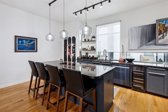 kitchen featuring a kitchen breakfast bar, beverage cooler, sink, light hardwood / wood-style flooring, and dishwasher