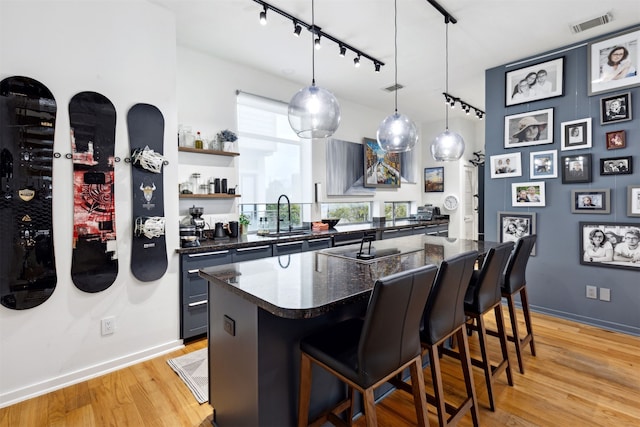 kitchen featuring a breakfast bar, track lighting, sink, hanging light fixtures, and light wood-type flooring