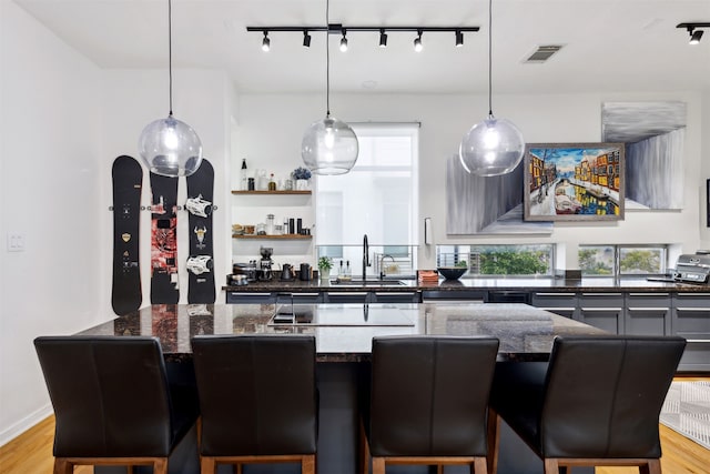 kitchen with track lighting, a kitchen breakfast bar, sink, light hardwood / wood-style flooring, and decorative light fixtures