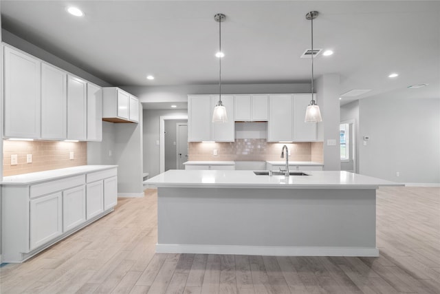 kitchen featuring an island with sink, white cabinetry, sink, and light hardwood / wood-style flooring