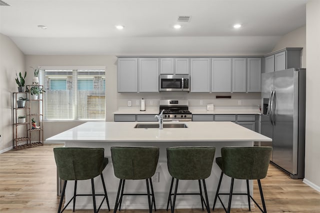 kitchen featuring a kitchen island with sink, light hardwood / wood-style flooring, stainless steel appliances, sink, and gray cabinets