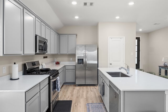 kitchen featuring stainless steel appliances, a center island with sink, sink, vaulted ceiling, and light hardwood / wood-style floors