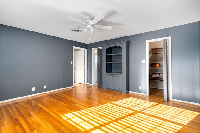 unfurnished bedroom featuring hardwood / wood-style flooring, ceiling fan, a walk in closet, and a closet