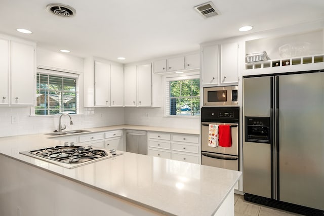 kitchen featuring kitchen peninsula, appliances with stainless steel finishes, a wealth of natural light, sink, and white cabinets