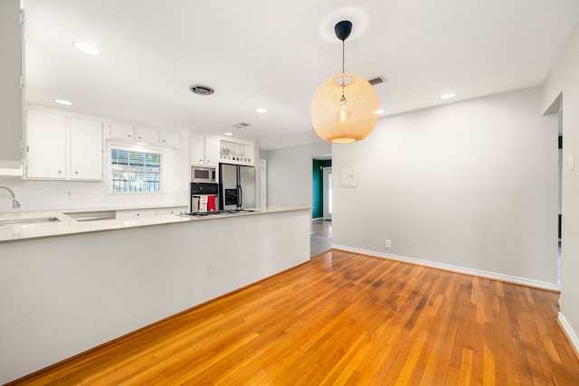 kitchen with white cabinetry, hanging light fixtures, stainless steel appliances, light hardwood / wood-style floors, and decorative backsplash