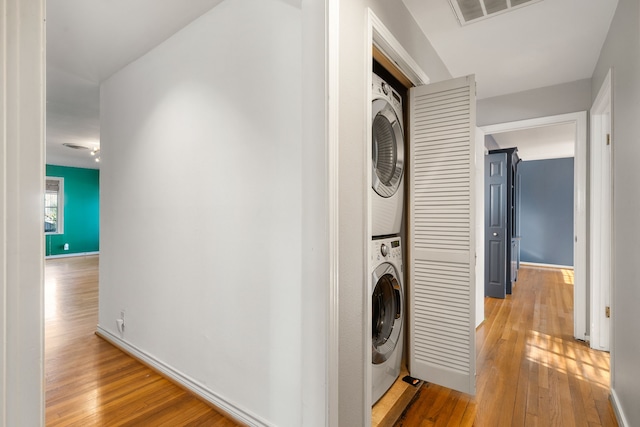 laundry room with stacked washing maching and dryer and light hardwood / wood-style flooring