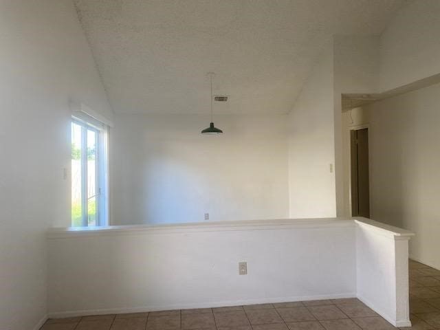 tiled empty room featuring vaulted ceiling