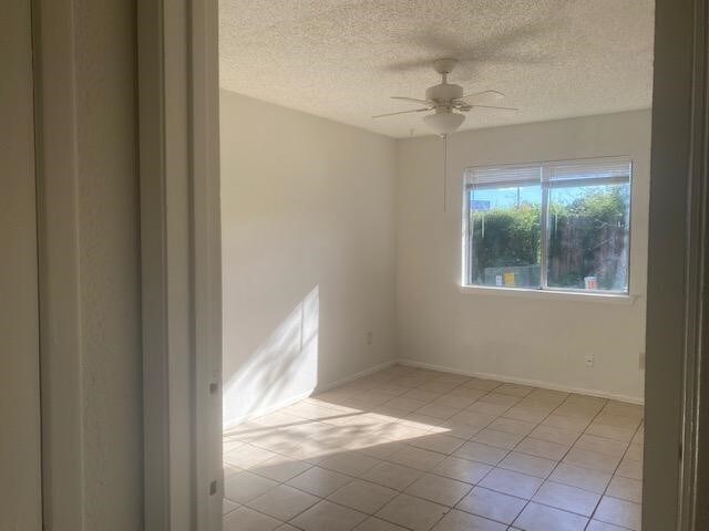 tiled empty room featuring ceiling fan and a textured ceiling