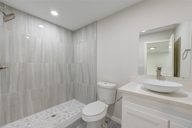 bathroom with a tile shower, wood-type flooring, vanity, and toilet