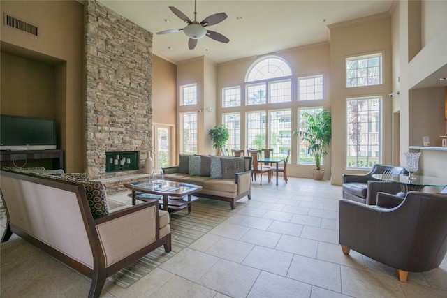 tiled living room featuring ceiling fan, a stone fireplace, a towering ceiling, and ornamental molding